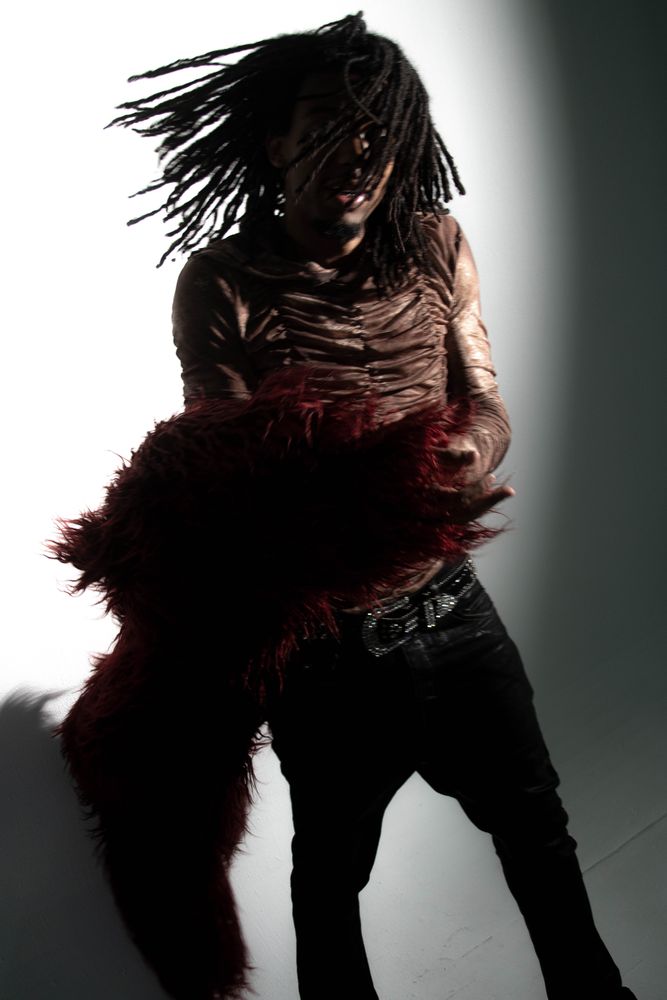 Steelo Fran spinning in a red fur coat, locs whipping across his face